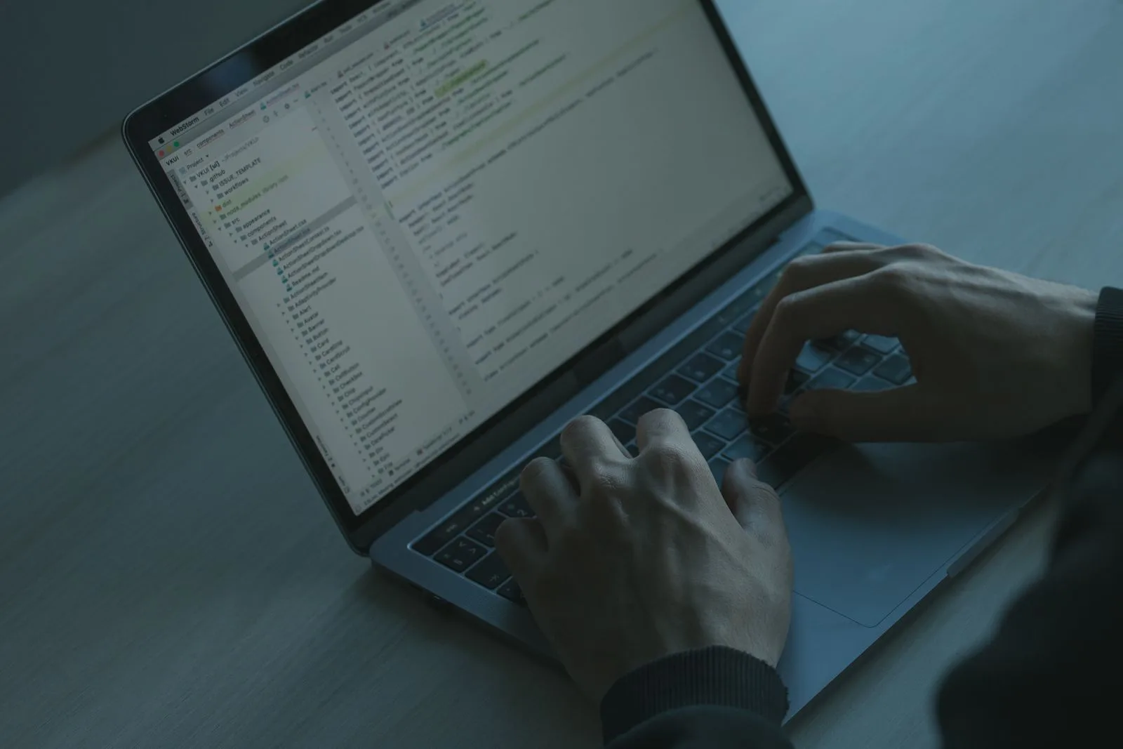 Person tippt auf einem Laptop, auf dem Bildschirm ist Programmcode zu sehen