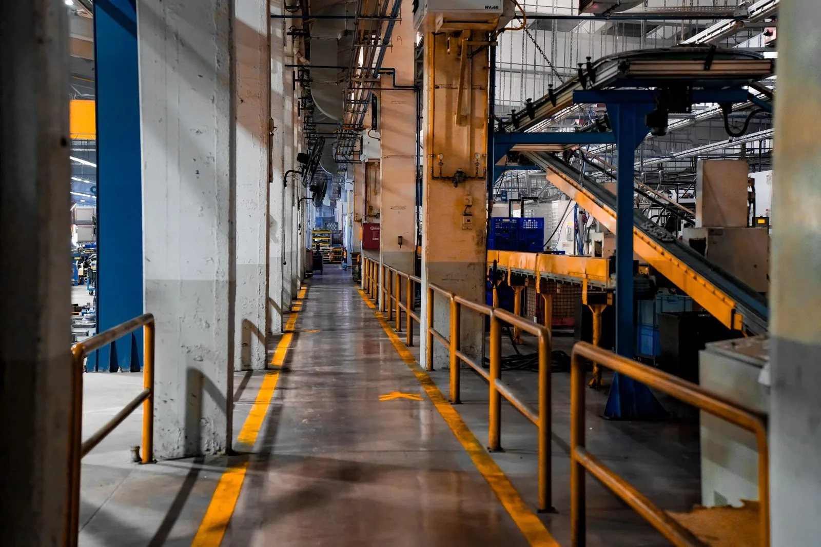 Lange Halle einer Fabrik mit Förderbändern, Stahlträgern und gelb markiertem Laufweg