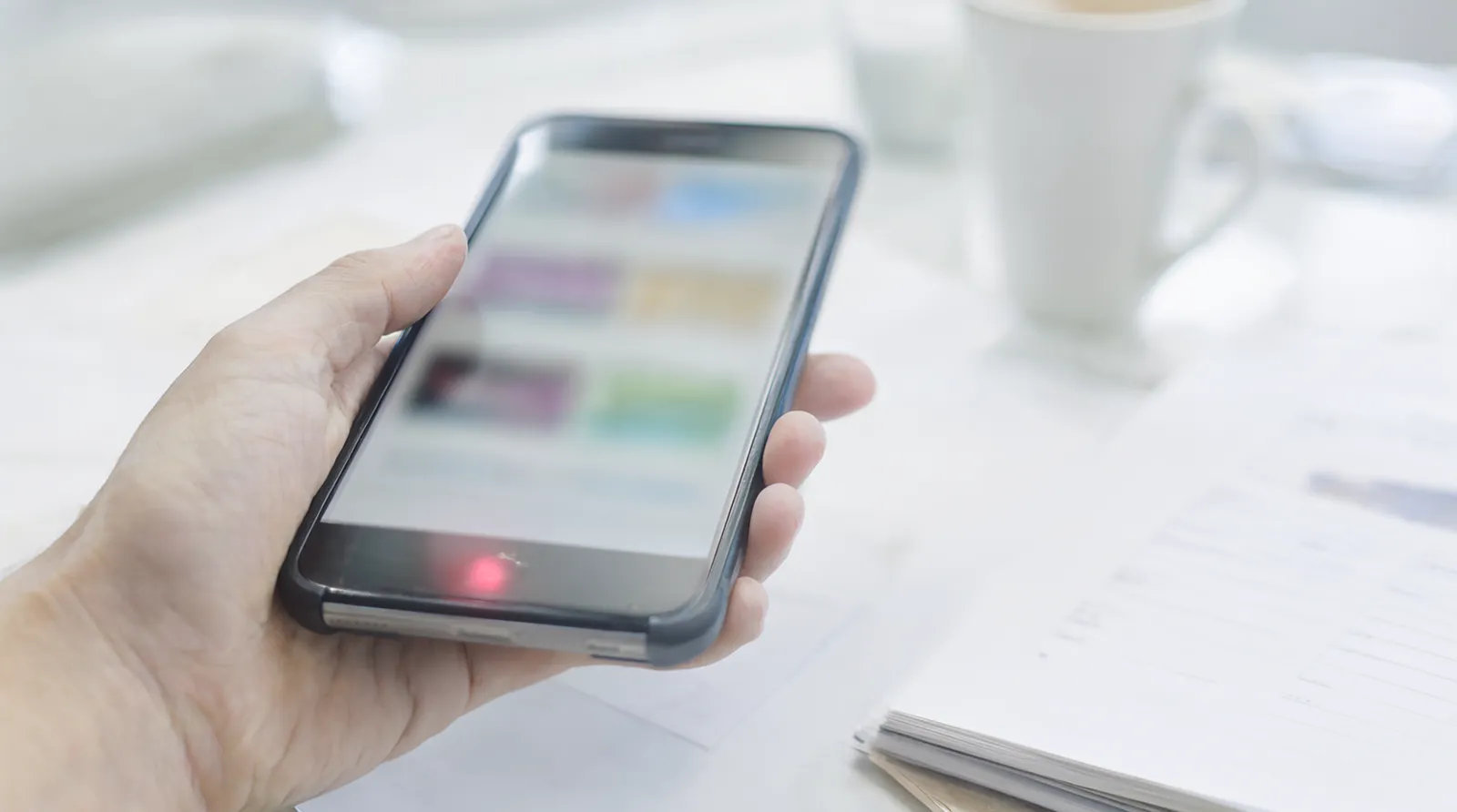 Hand hält ein Smartphone mit unscharfem, buntem Bildschirminhalt über einem hellen Schreibtisch