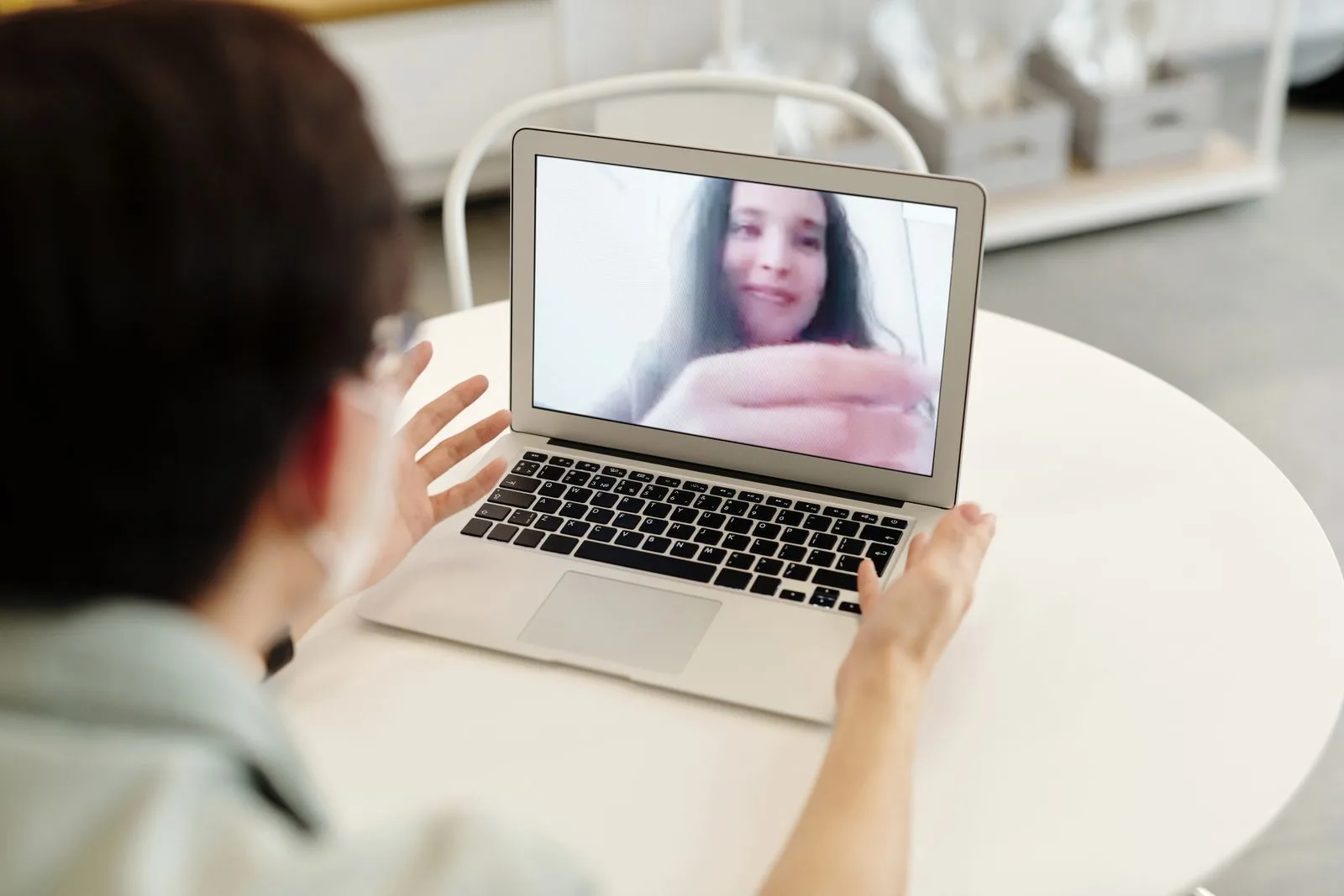 Person sitzt vor einem Laptop und spricht per Videoanruf mit einer lächelnden Frau auf dem Bildschirm