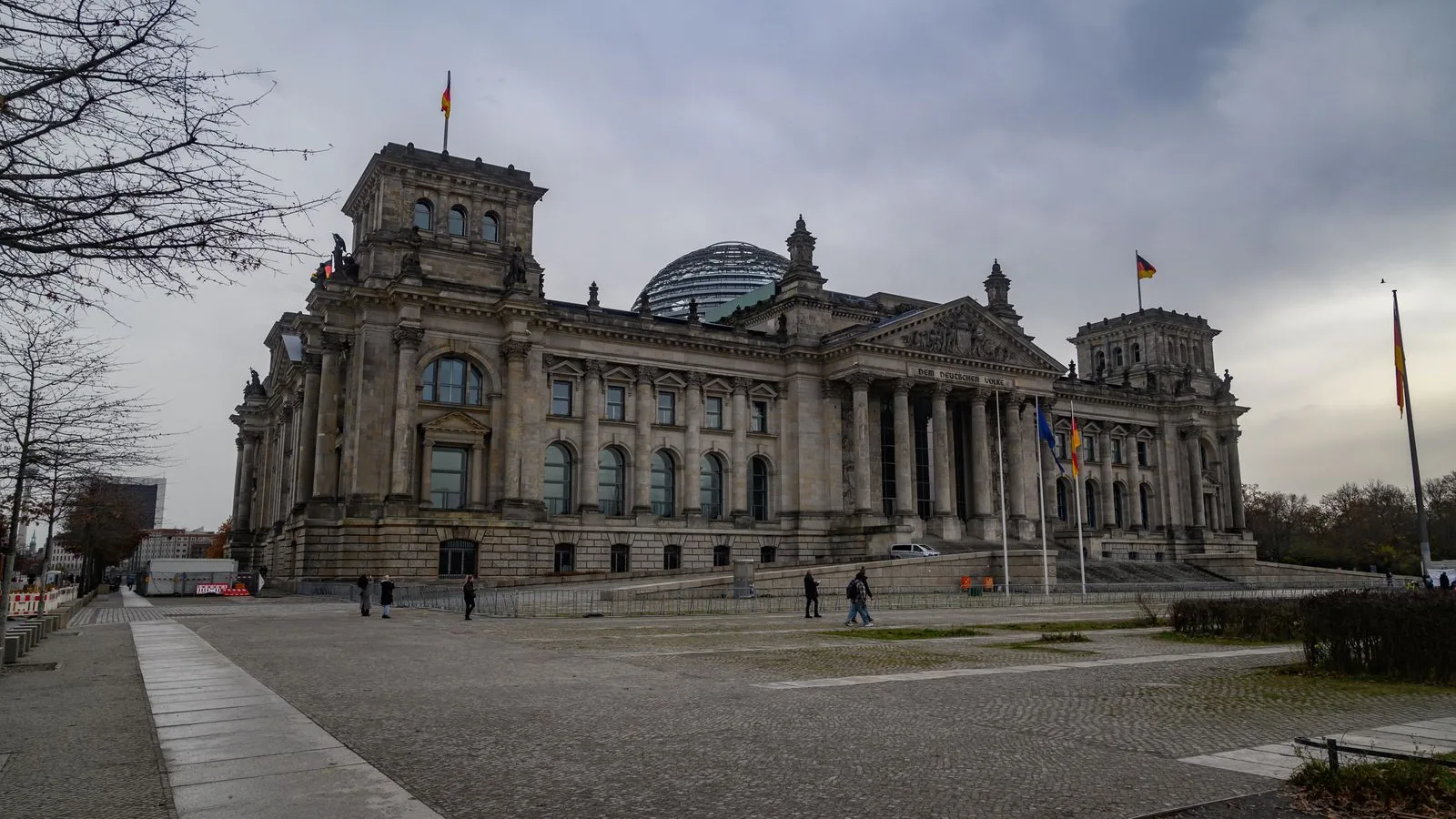 Das Reichstagsgebäude in Berlin an einem grauen Wintertag, seitlicher Blick auf die Säulenfront mit der gläsernen Kuppel und wehenden Flaggen