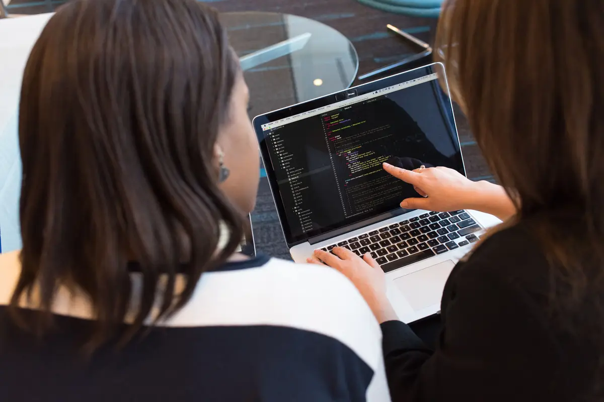 Zwei Entwicklerinnen prüfen gemeinsam Code an einem Bildschirm