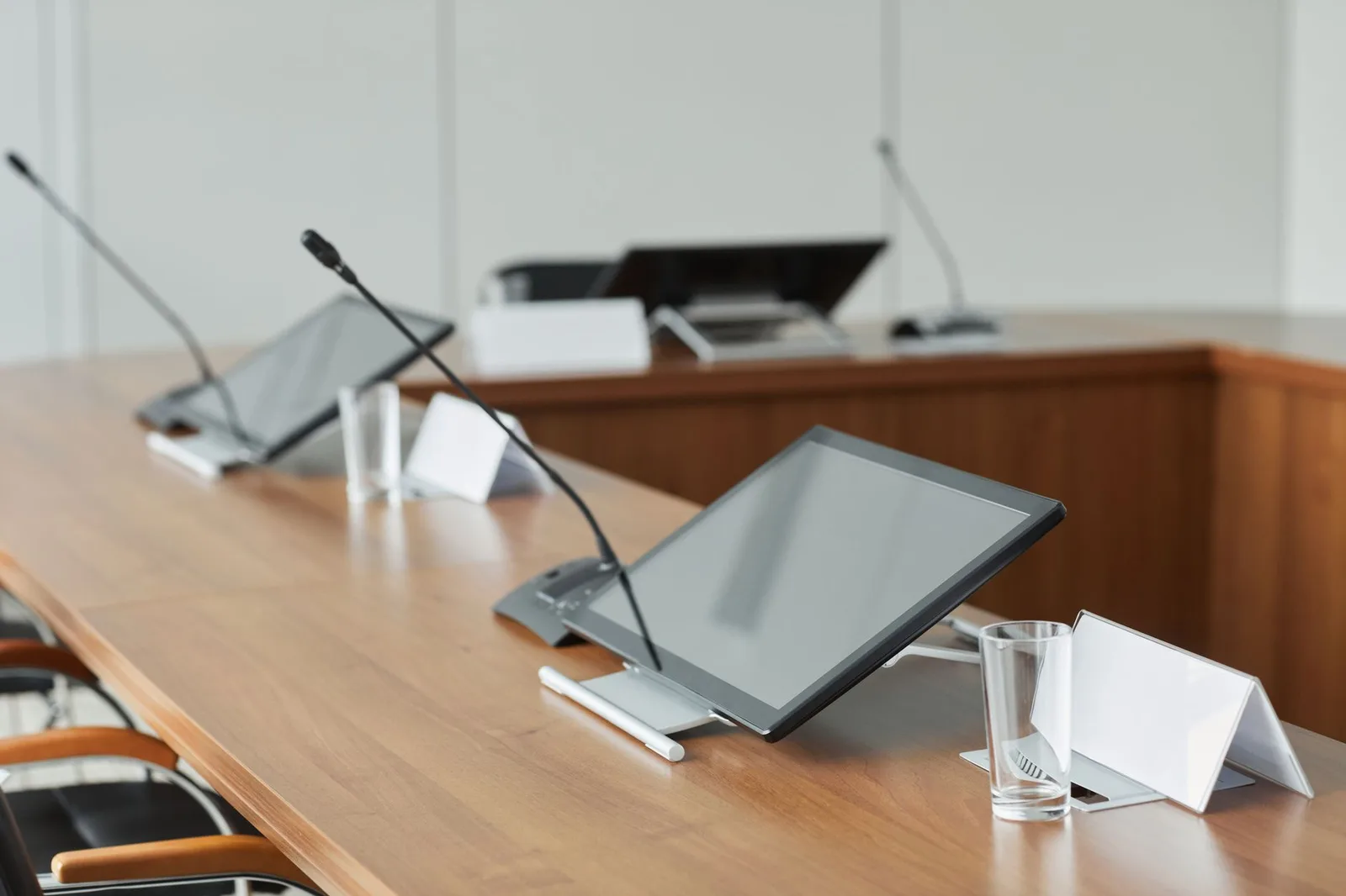 Moderner Konferenzraum mit Tischmikrofonen und Bildschirmen auf einem Holztisch