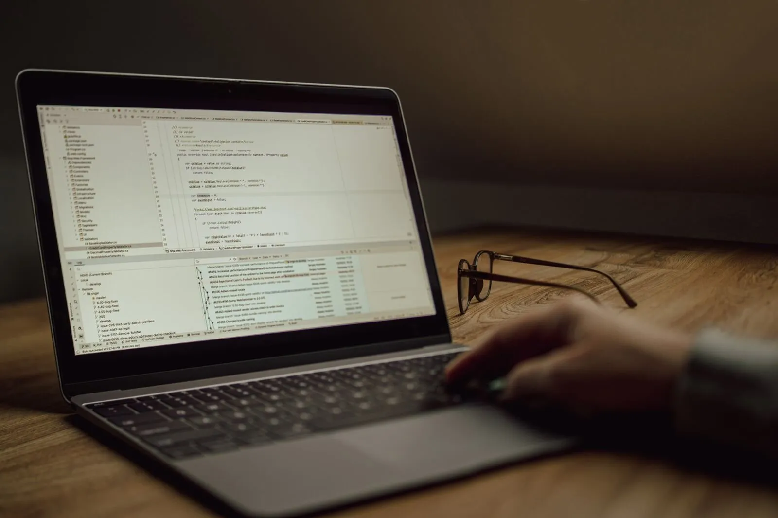 Person programmiert an einem Laptop, daneben liegt eine Brille auf dem Tisch