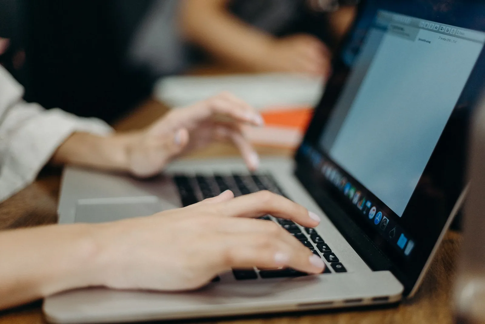 Hände tippen an einem Laptop in einem Büro, im Hintergrund eine zweite Person