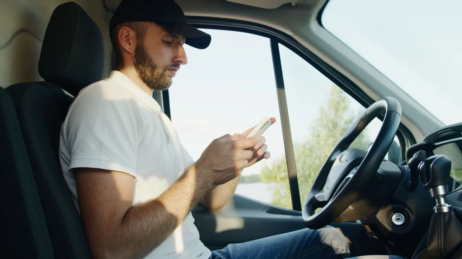 Fahrer sitzt am Steuer eines geparkten Autos und blickt auf sein Smartphone